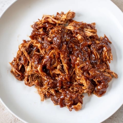 A slow cooker full of richly sauced BBQ pulled chicken, smoky and ready to be shredded.