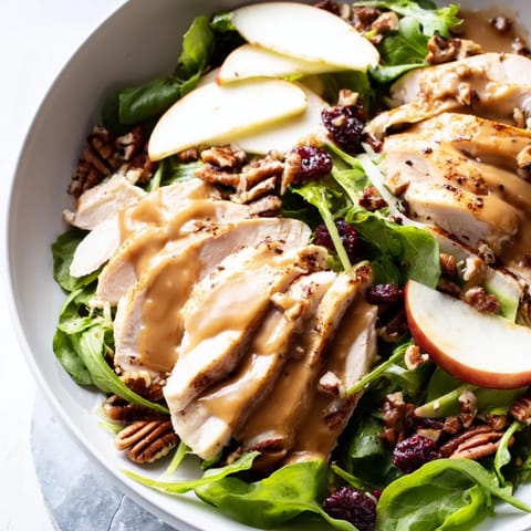 A close-up of Caramel Apple Chicken Salad features feta crumbles and cranberries, drizzled with glossy caramel-pecan dressing.