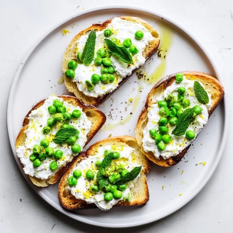 A close-up of Pea & Mint Ricotta Toast spread thick on toasted sourdough, garnished with chopped mint and lemon wedges.