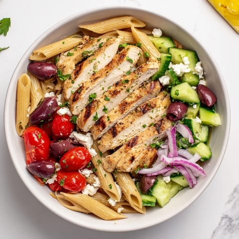 Tender slices of marinated chicken top a colorful Greek Chicken Pasta Bowl with fresh parsley and red onion.
